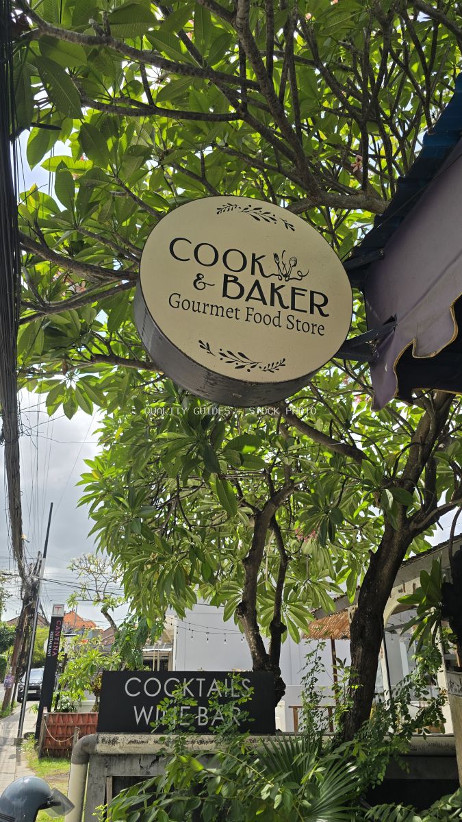 Circular 'Cook & Baker Gourmet Food Store' sign surrounded by green trees in Bali. - stock photo