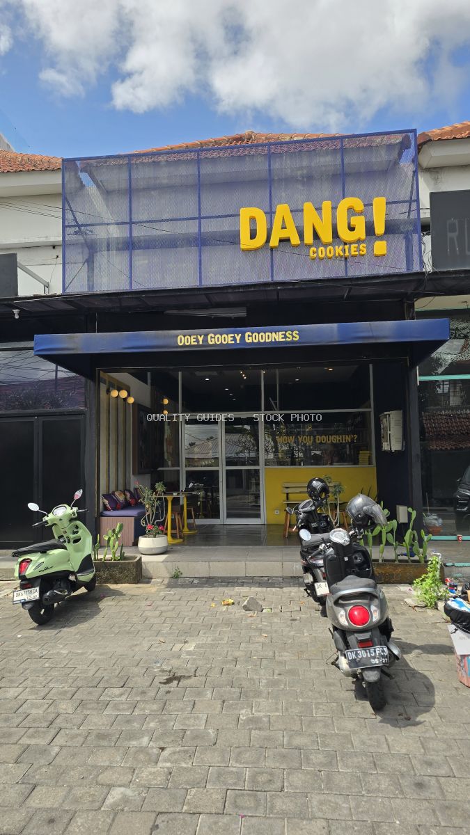 Exterior of Dang! Cookies shop in Bali with yellow and blue sign, scooters parked outside on a sunny day. - stock photo
