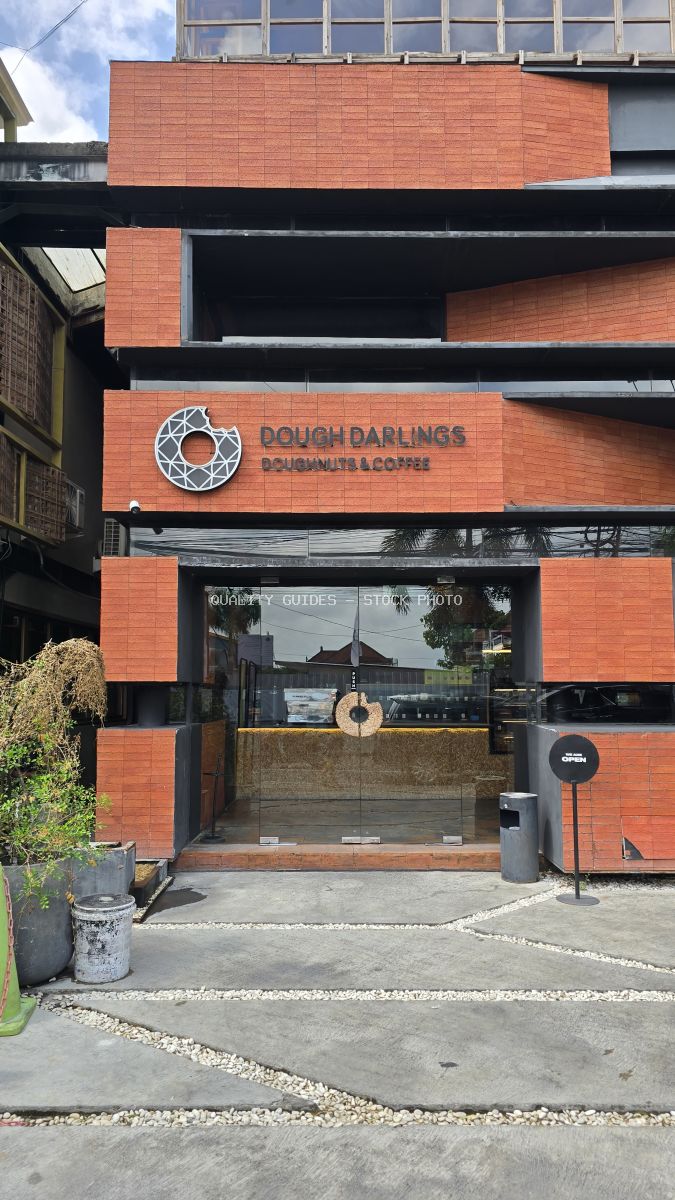 Exterior of Dough Darlings cafe in Canggu, Bali, with terracotta brick facade, glass entrance, and 'Doughnuts & Coffee' sign. - stock photo