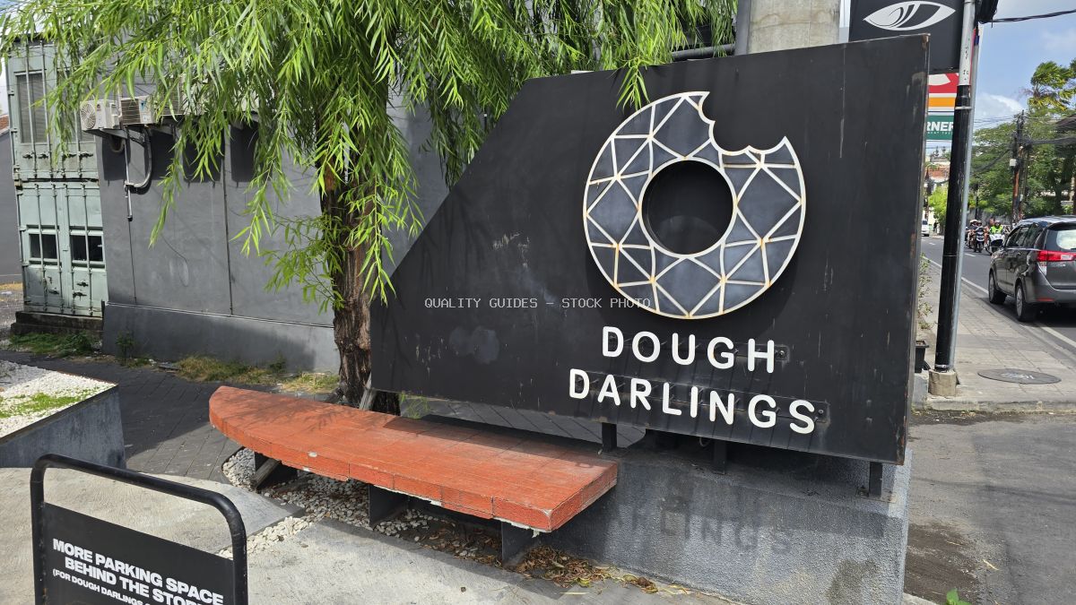 Black sign for Dough Darlings donut shop in Canggu, Bali, with a geometric donut logo and a wooden bench. - stock photo