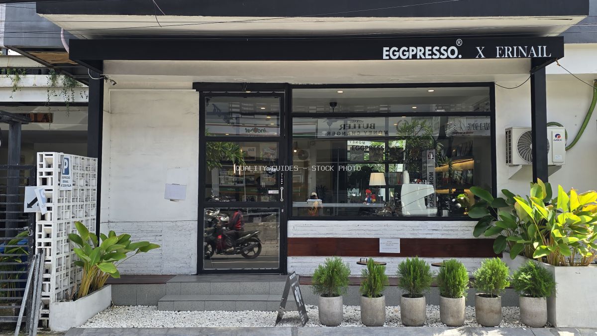 Exterior of Eggpresso cafe and Erinail salon in Canggu, Bali, with white walls, black windows, and green plants. - stock photo