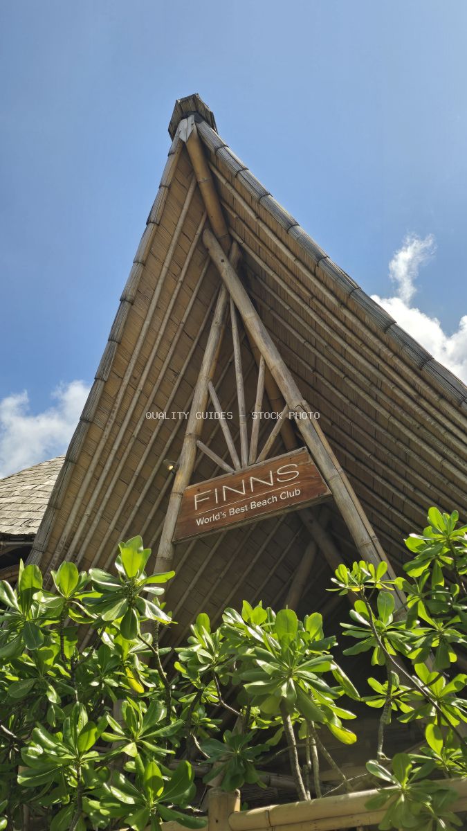 Finns Beach Club entrance in Bali, featuring a unique bamboo and thatched roof structure with a 'World's Best Beach Club' sign, set against a clear blue sky. - stock photo