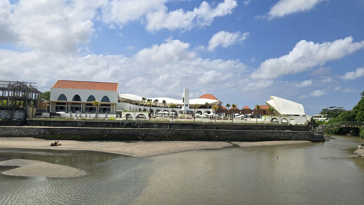 Exterior view of Café del Mar Bali, a white resort complex with terracotta roofs by a river under a blue sky. - stock photo