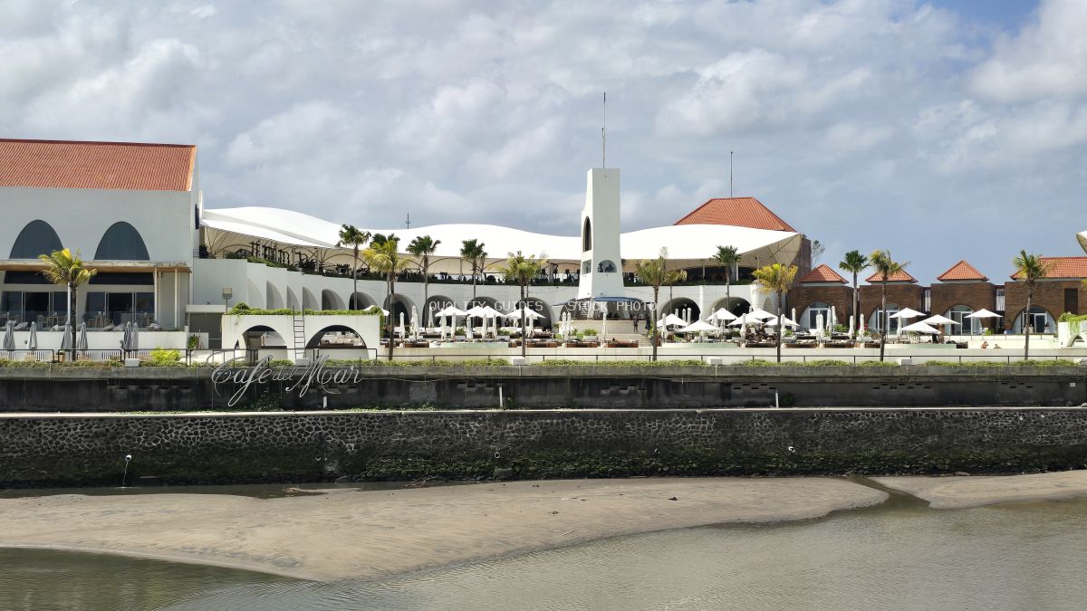 Exterior view of Cafe del Mar Bali beach club with white buildings, terracotta roofs, palm trees, and umbrellas. - stock photo