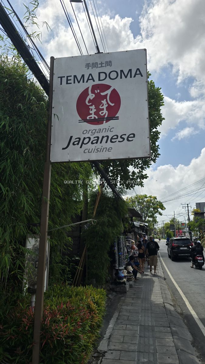 Sign for Tema Doma organic Japanese cuisine restaurant on a street in Bali with people and traffic. - stock photo