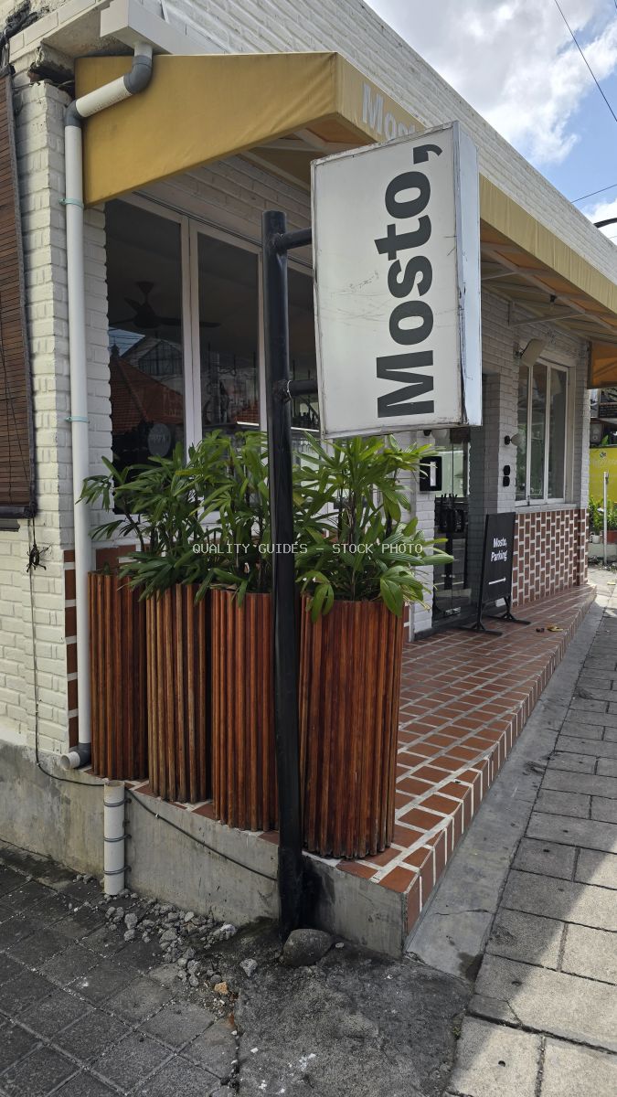 Exterior view of Mosto restaurant in Berawa, Bali, with a yellow awning, white brick, and green plants. - stock photo