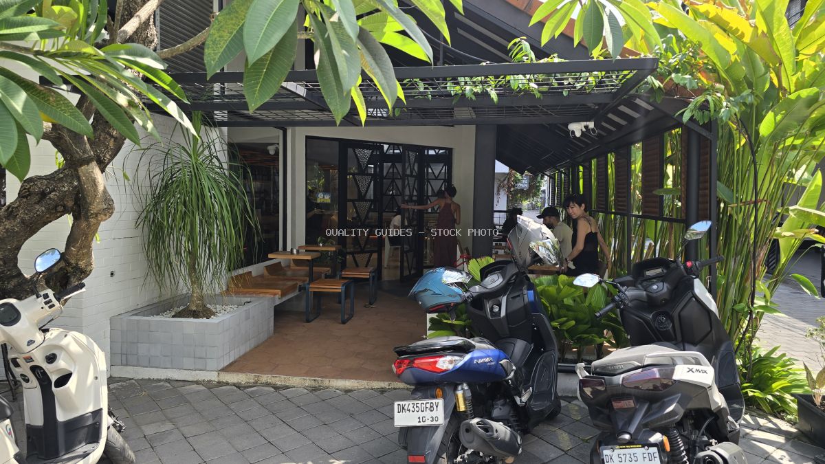 Exterior of a modern tropical cafe in Bali with outdoor seating, lush plants, parked scooters, and people. - stock photo