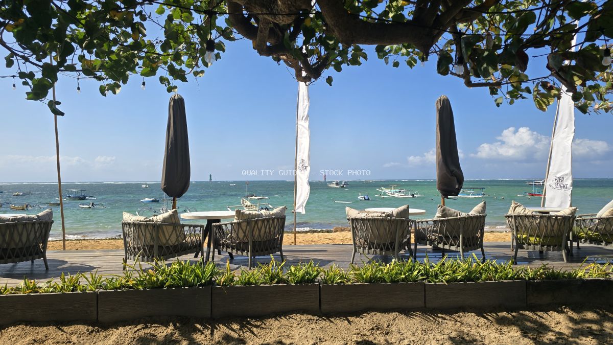 Empty beachfront restaurant with wicker chairs, tables, and a view of the turquoise ocean with boats under a clear blue sky in Bali. - stock photo