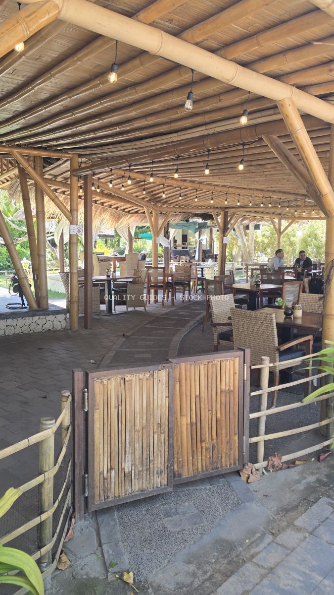 Outdoor cafe with bamboo roof, wicker furniture, and string lights in a tropical setting. - stock photo