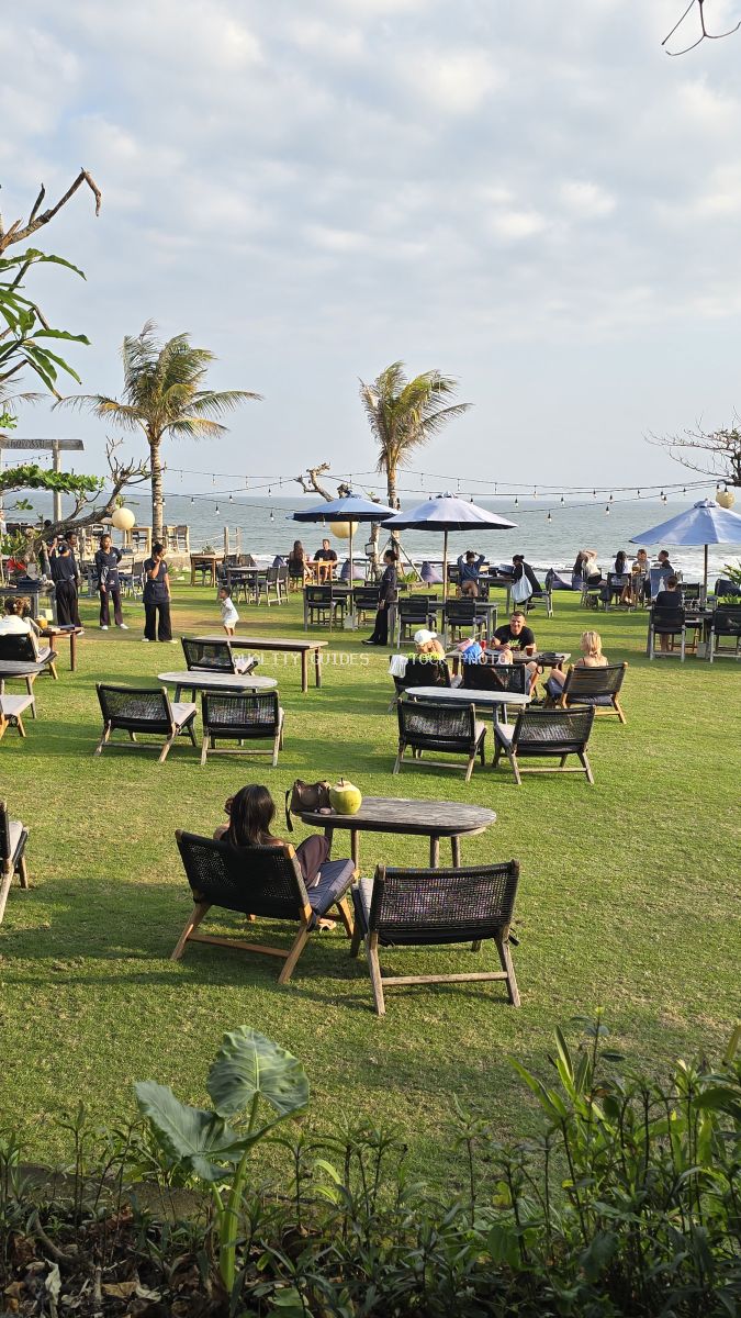 People dining outdoors at a vibrant beachfront restaurant with palm trees and ocean views in Bali. - stock photo