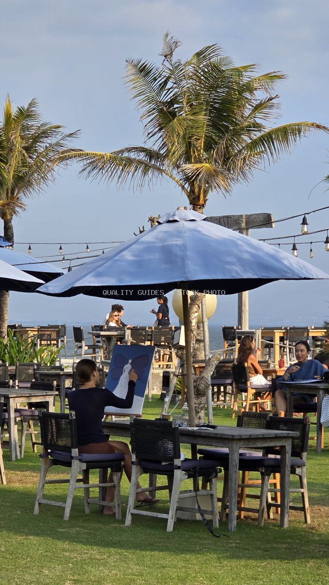 Person painting at an outdoor cafe with palm trees and ocean view in Bali. - stock photo