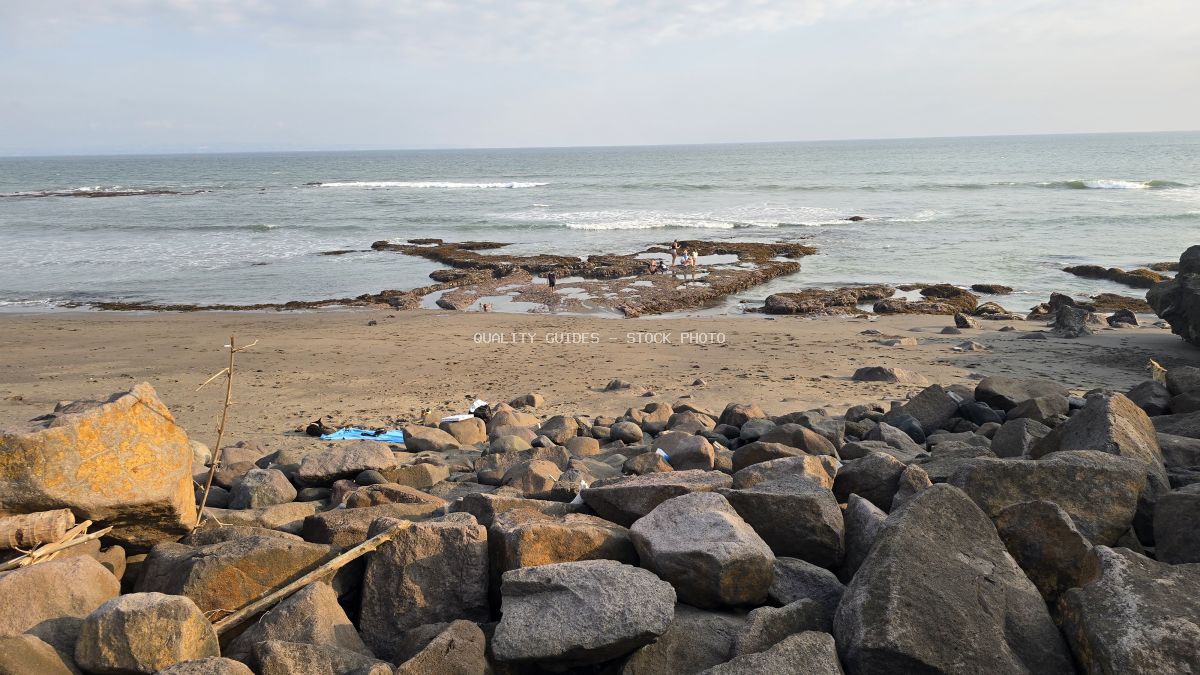 Rocky Seseh Beach in Bali with ocean waves, tide pools, and distant people exploring. - stock photo