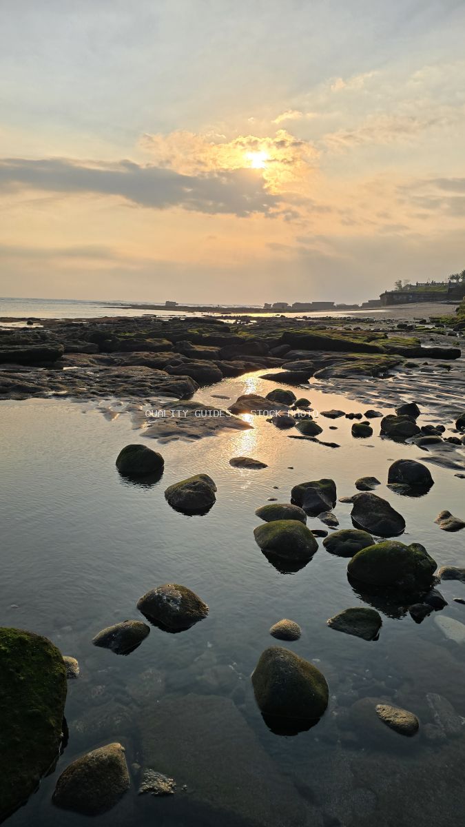 Golden sunset reflecting on tide pools and mossy rocks at Cemagi Beach, Bali. - stock photo