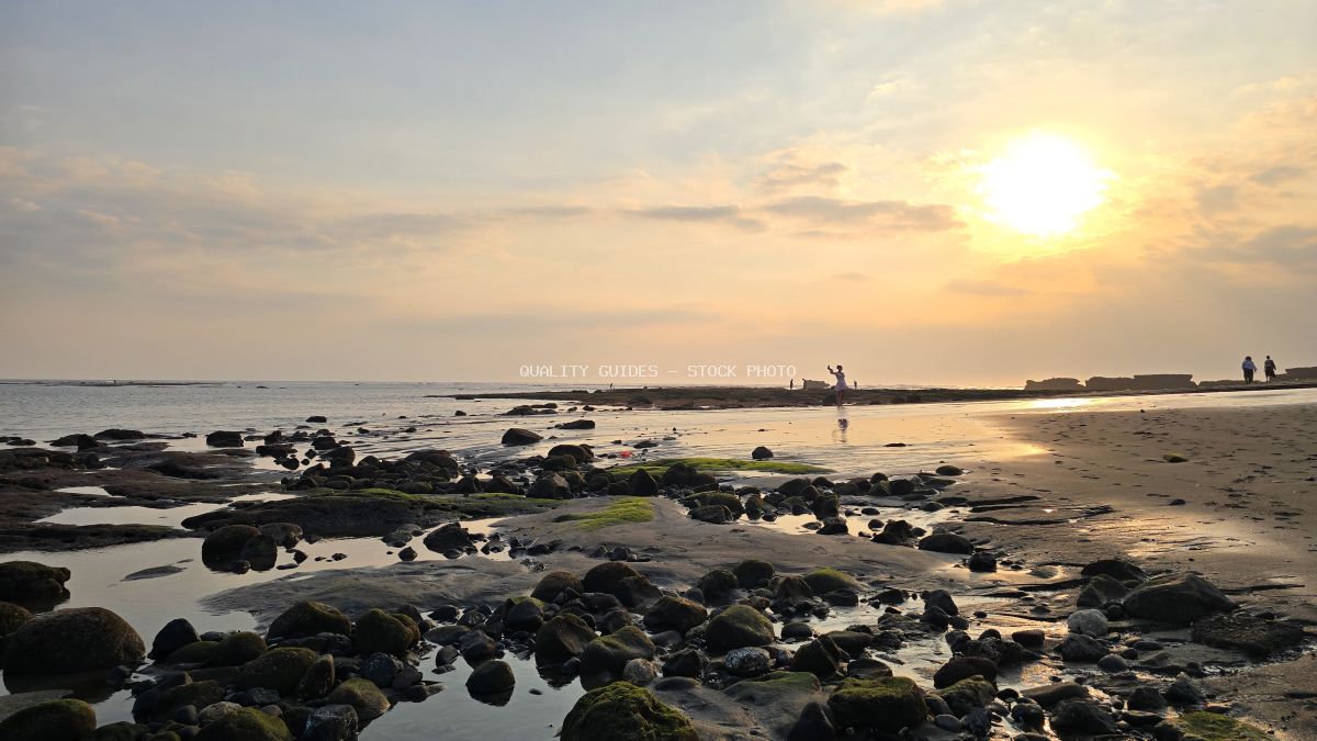 Sunset over Cemagi Beach in Bali with rocky foreground and silhouetted people enjoying the view. - stock photo