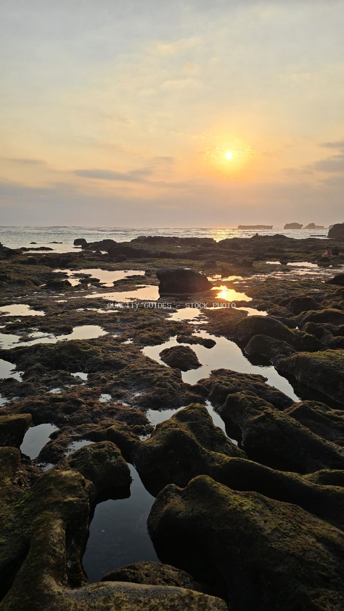 Sunset over a rocky beach with tide pools reflecting golden light, Cemagi Beach, Bali. - stock photo