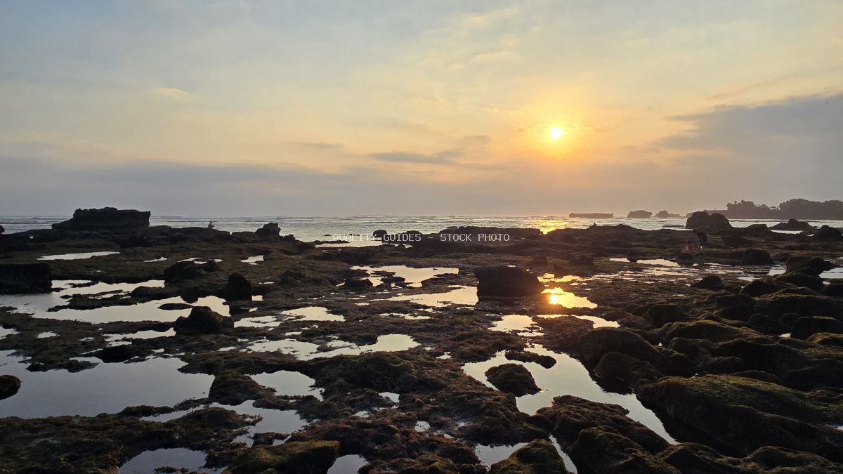 Golden sunset over a rocky beach with tide pools and ocean waves at Cemagi Beach, Bali. - stock photo
