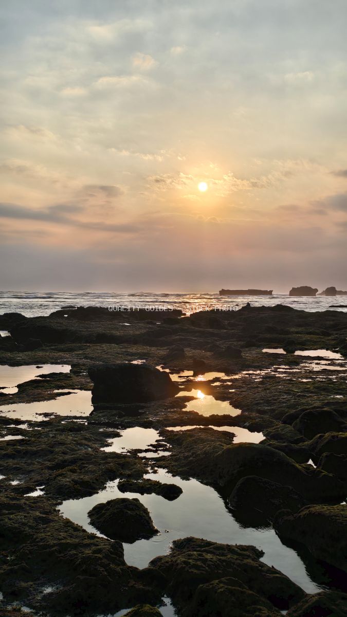 Sunset over a rocky beach with tide pools reflecting the golden sun and cloudy sky. - stock photo