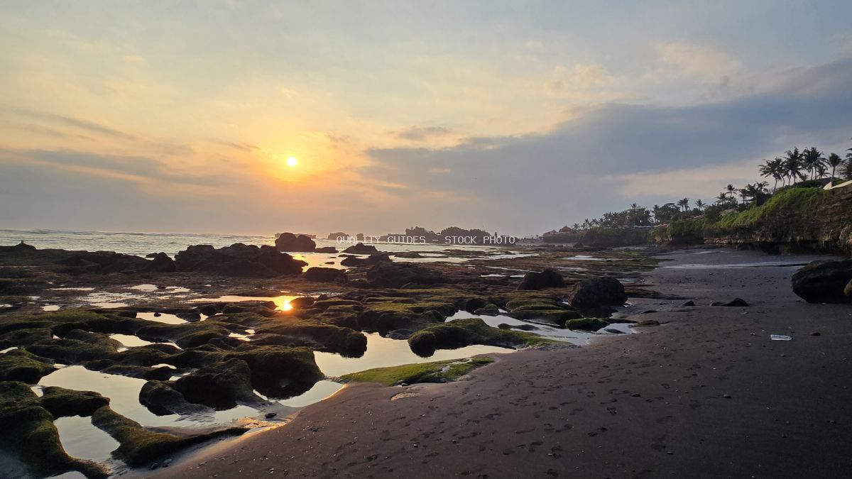 Sunset over Cemagi Beach, Bali, with golden light reflecting in tidal pools and dark rocks. - stock photo
