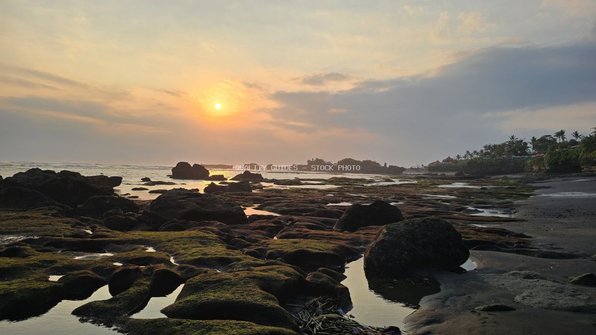 Sunset over Mengening Beach in Bali, showing a rocky coastline with tidal pools and golden sky. - stock photo