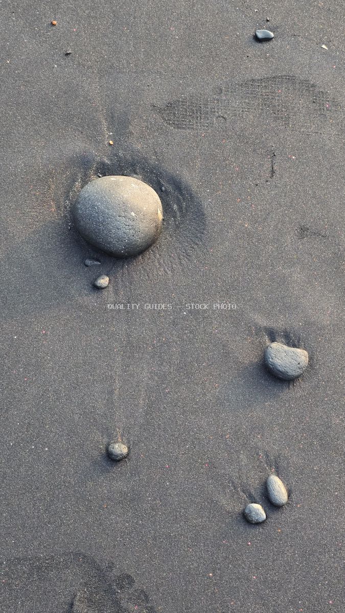 Close-up of black sand beach with smooth grey pebbles. - stock photo