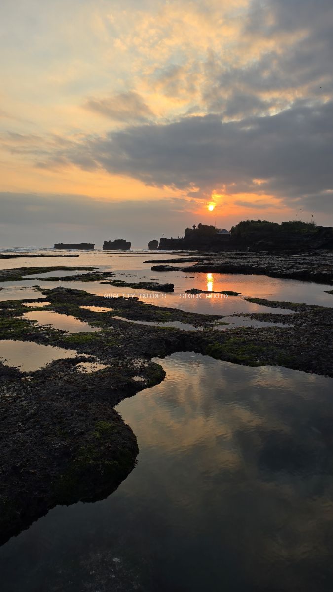Sunset at Mengening Beach, Bali, with rocky tide pools reflecting the colorful sky and distant rock formations. - stock photo