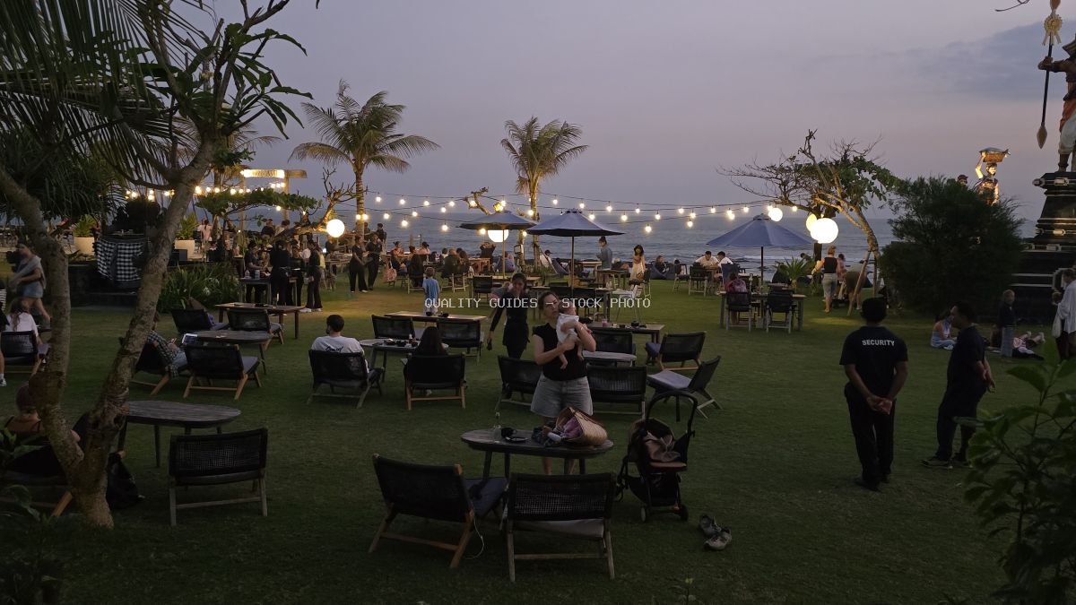 People enjoying an evening at a beach club on Seseh Beach, Bali, with string lights and palm trees. - stock photo