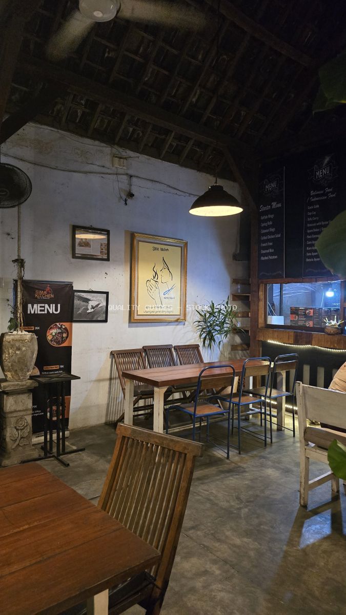 Interior of Sima Kitchen restaurant in Bali with rustic wooden furniture, dim lighting, and a menu banner. - stock photo
