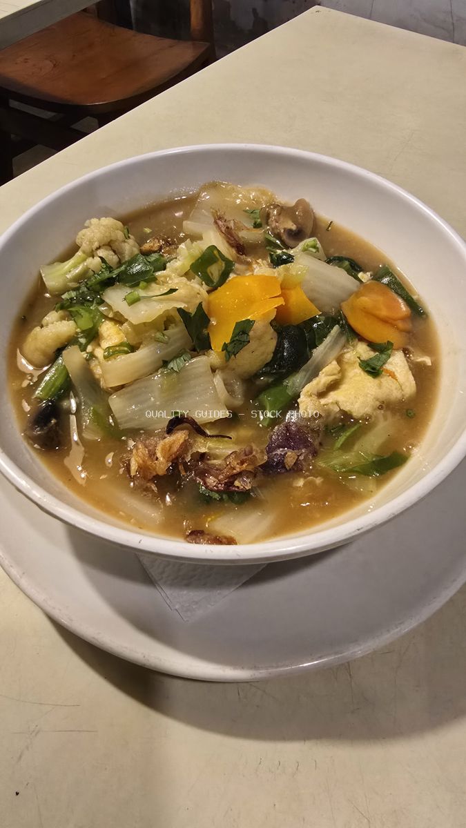 Close-up of a bowl of Indonesian vegetable soup with tofu, cauliflower, cabbage, and carrots on a table. - stock photo