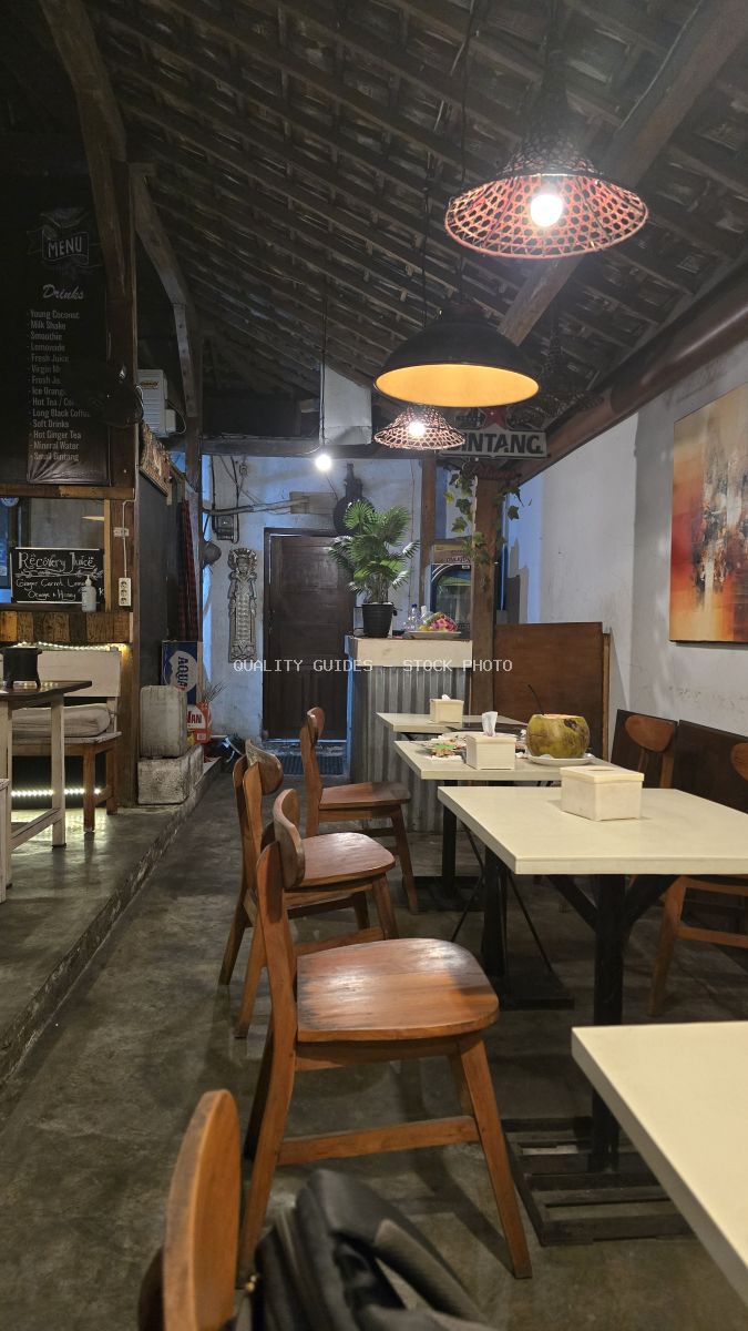 Interior view of a rustic Balinese cafe with wooden furniture, ambient lighting, and a coconut drink on a table. - stock photo