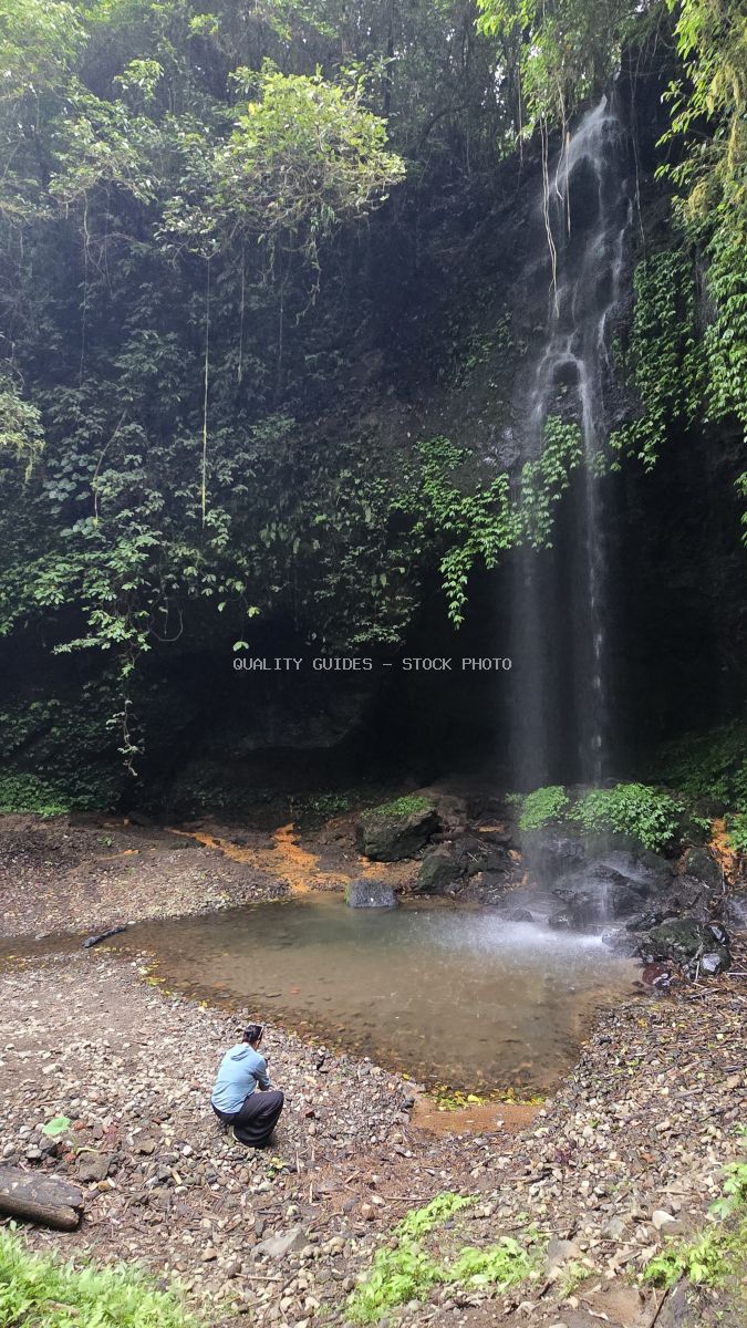 Solo traveler at Banyu Wana Amertha Waterfall in Bali, Indonesia, with cascading waterfall and lush jungle vegetation - stock photo