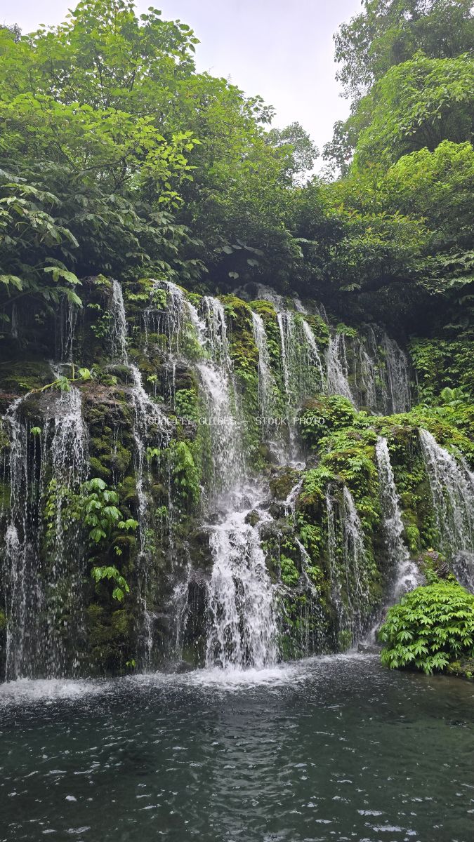 Banyu Wana Amertha Waterfall in Bali with cascading water over moss-covered rocks surrounded by lush tropical forest - stock photo