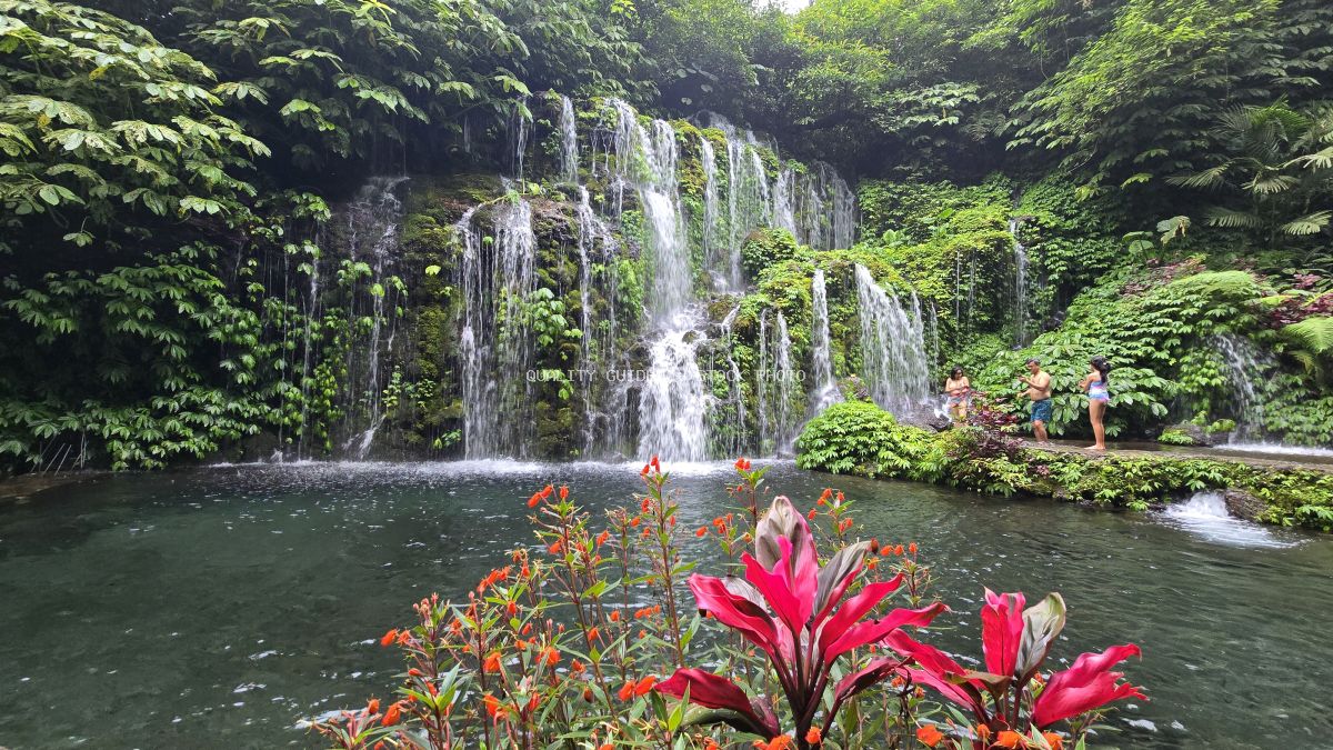 Banyu Wana Amertha Waterfall in Bali with cascading water, emerald pool, red tropical flowers, and lush jungle vegetation - stock photo