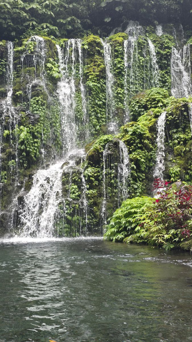 Multi-tiered waterfall with moss-covered columnar rocks and emerald pool in Bali tropical rainforest - stock photo