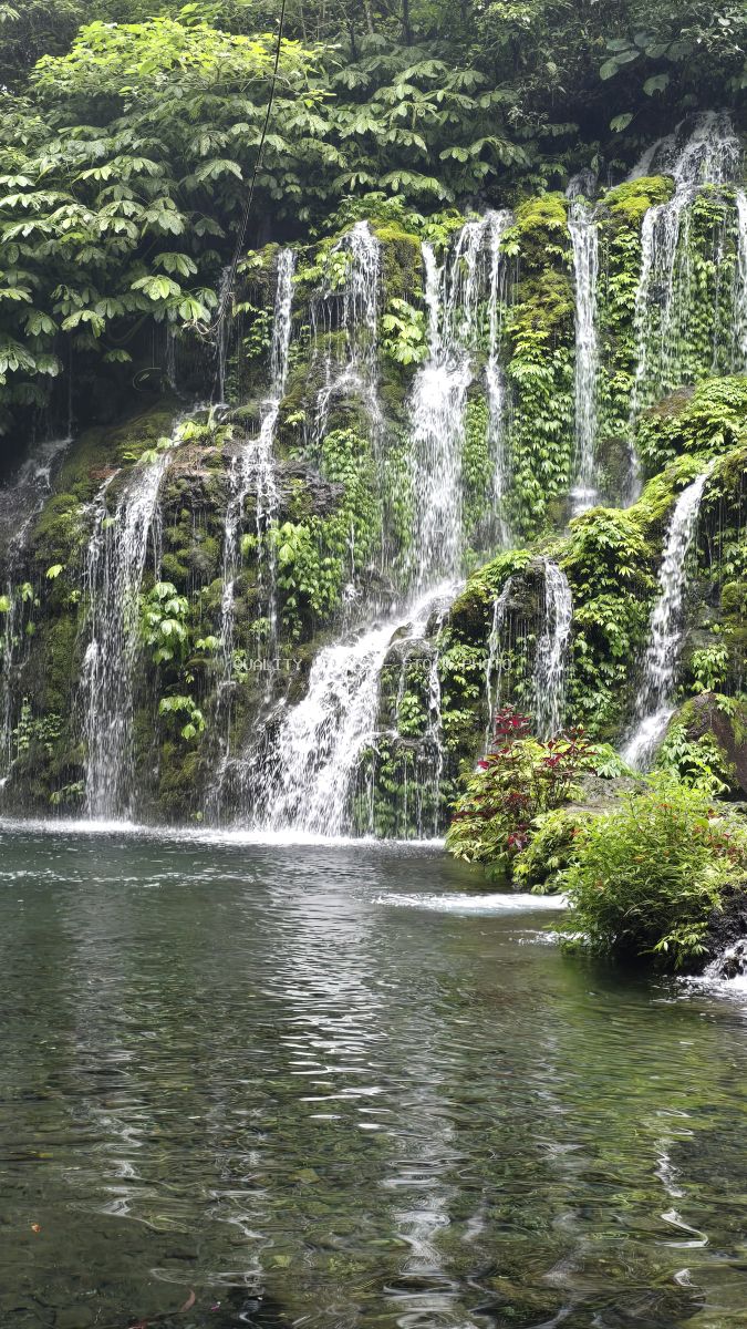 Multi-tiered waterfall with white water streams cascading down moss-covered rocks surrounded by lush green tropical jungle and emerald pool in Bali - stock photo
