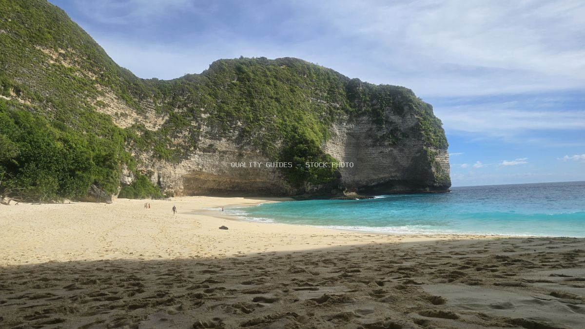 Kelingking Beach in Bali with turquoise waters, white sand, and dramatic green-covered limestone cliffs - stock photo