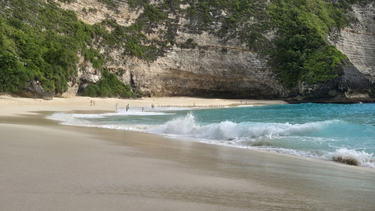 Kelingking Beach Bali with turquoise waters, white sand, and dramatic limestone cliffs covered in green vegetation - stock photo