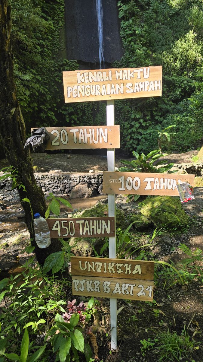 Wooden age decomposition sign at Pucak Manik Waterfall in Bali with waterfall and tropical vegetation - stock photo
