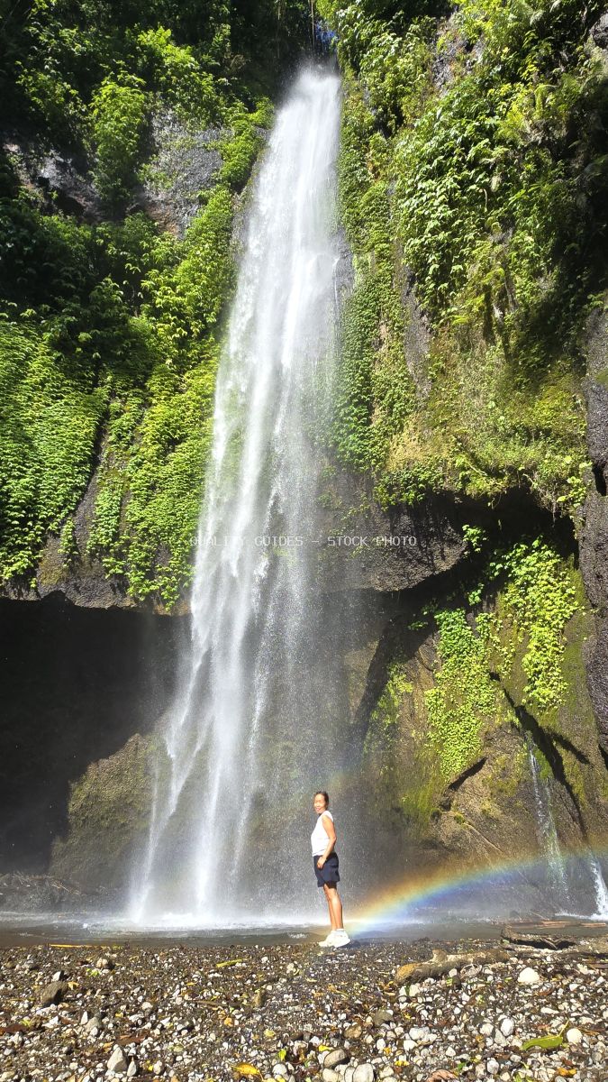 Solo traveler standing at Pucak Manik Waterfall in Bali with rainbow in waterfall mist - stock photo