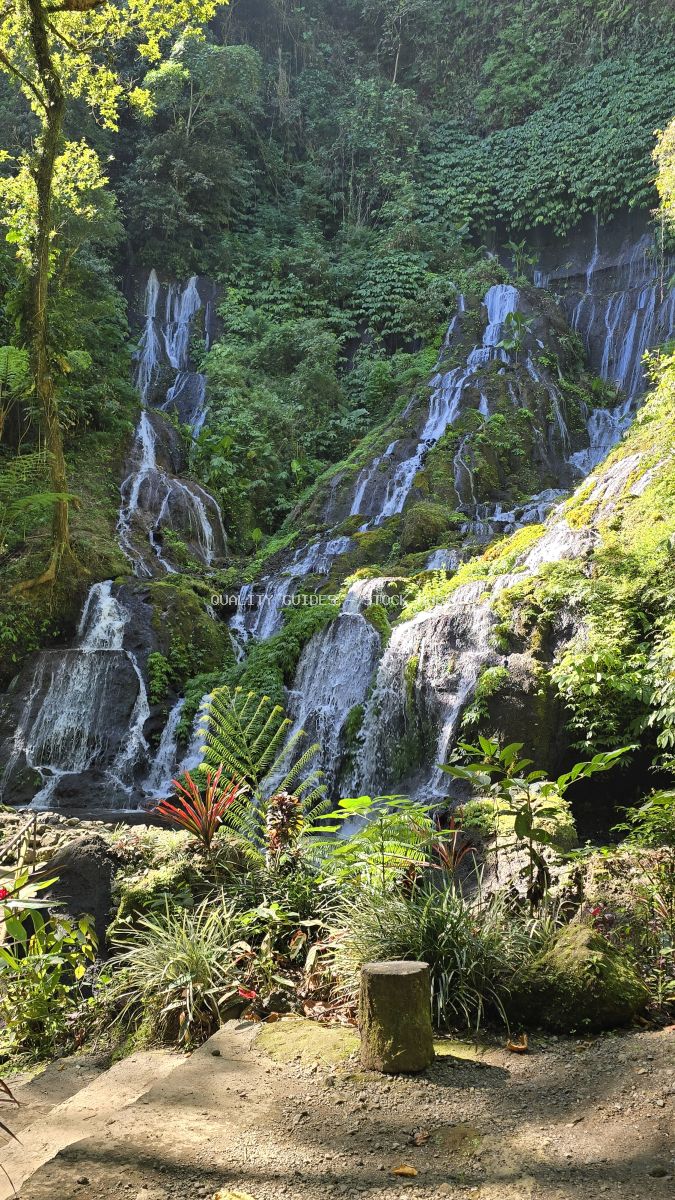 Multi-tiered waterfall flowing through lush tropical jungle with moss-covered rocks and vibrant green vegetation in Bali - stock photo