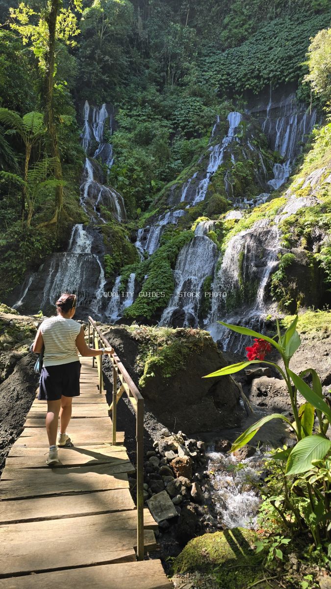 Hiker on wooden boardwalk at Pucak Manik Waterfall in Bali with cascading waterfalls and tropical jungle vegetation - stock photo
