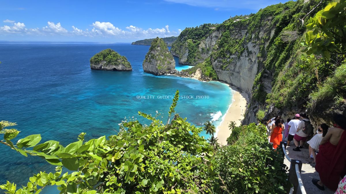 Aerial view of Diamond Beach Bali with turquoise waters, white sand, limestone cliffs, and tourists on clifftop viewpoint - stock photo