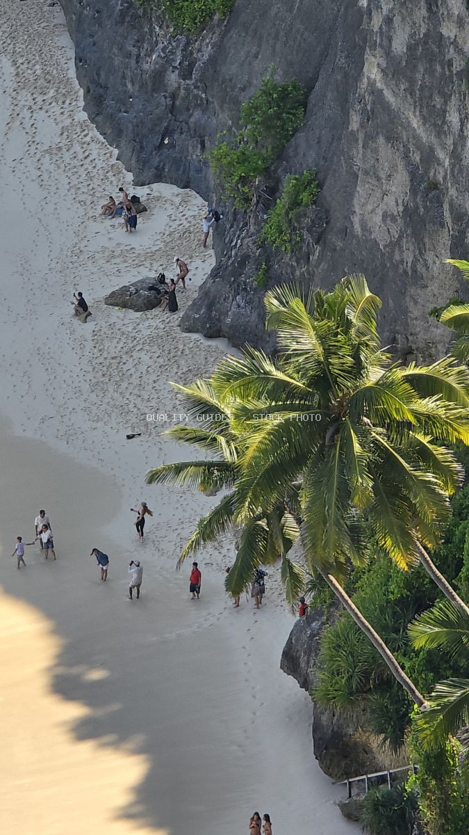 Aerial view of Diamond Beach Bali with tourists, white sand, limestone cliffs, and tropical palm trees - stock photo
