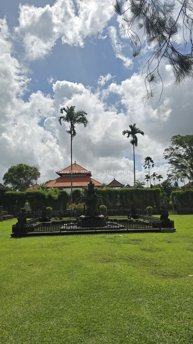 Taman Ayun Temple in Bali with tiered roof, coconut palms, and dramatic tropical sky - stock photo