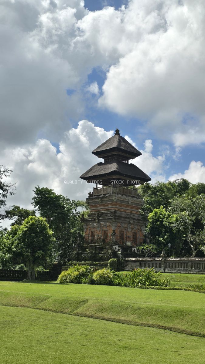 Taman Ayun Temple in Bali with traditional tiered pagoda roof, green lawns, and tropical sky with white clouds - stock photo