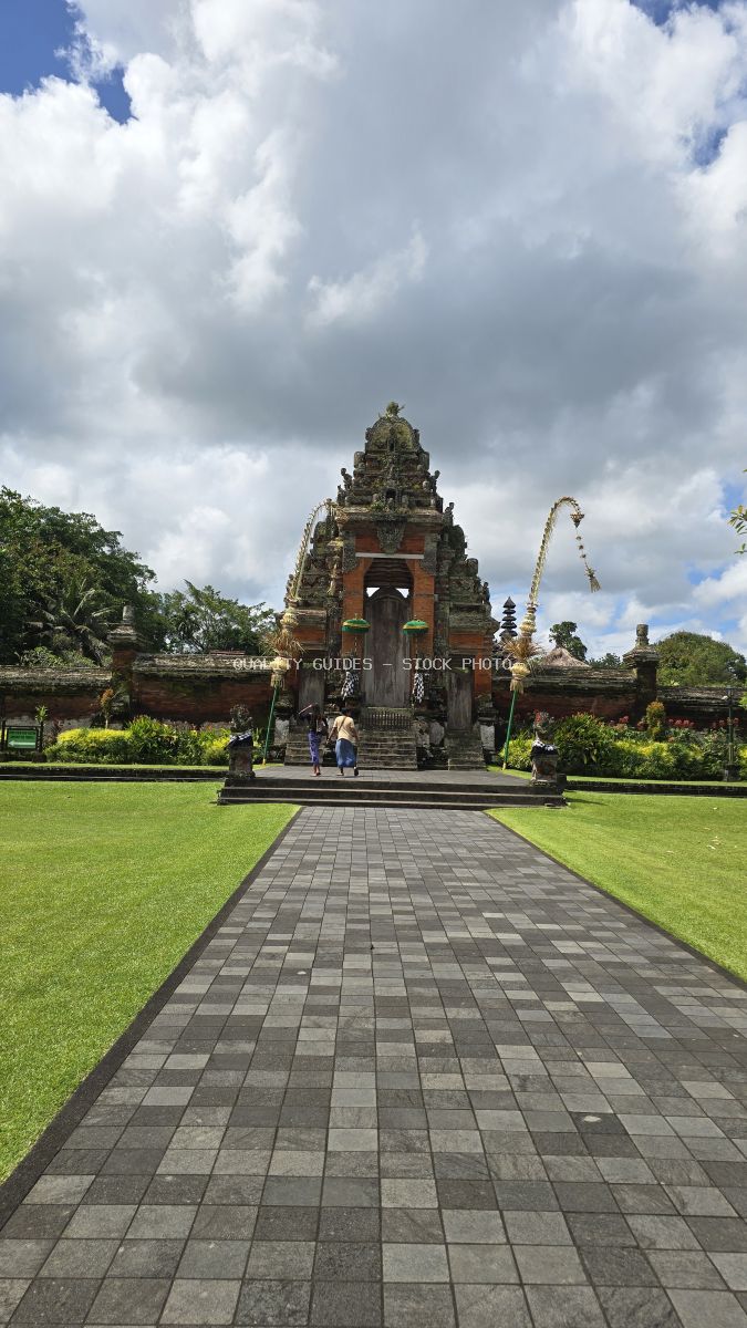 Taman Ayun Temple in Bali with ornate stone gateway, manicured lawns, and dramatic cloudy sky - stock photo