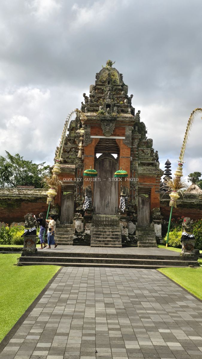 Ornate stone temple gate at Taman Ayun Temple in Bali with carved details, red brick archway, and manicured lawn - stock photo