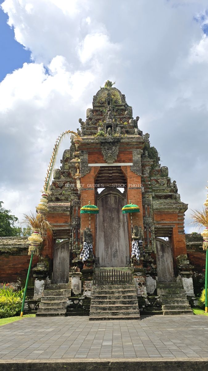 Taman Ayun Temple gateway in Bali with traditional stone architecture, ceremonial guardians, and tropical sky - stock photo