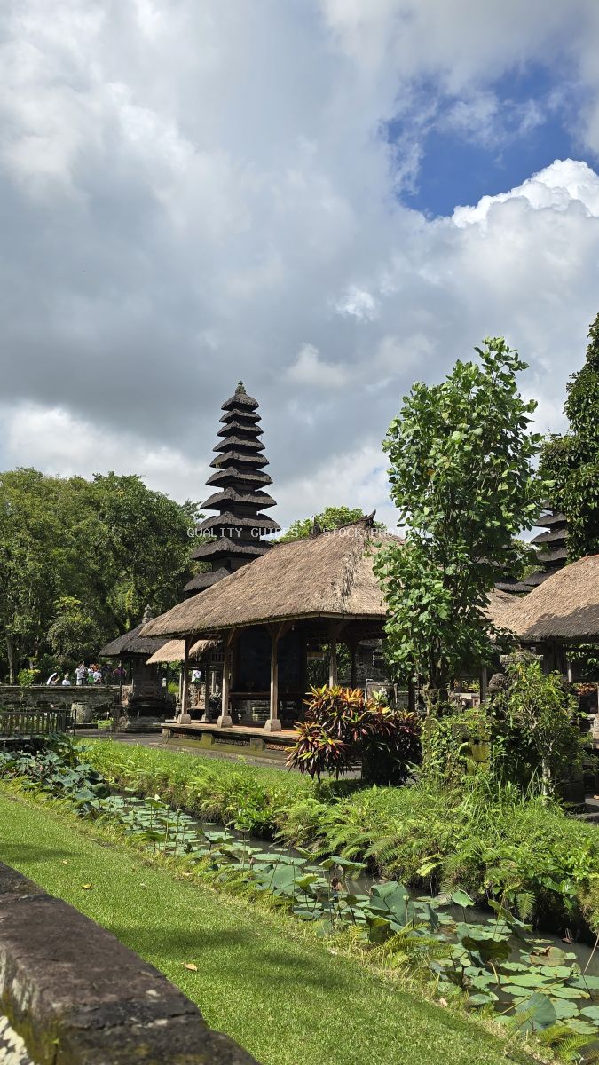 Taman Ayun Temple in Bali with traditional tiered pagoda, thatched pavilion, and lush tropical gardens under blue sky - stock photo