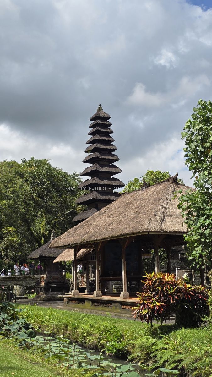 Taman Ayun Temple in Bali with tiered pagoda tower, thatched pavilion, and tropical pond surrounded by lush vegetation - stock photo