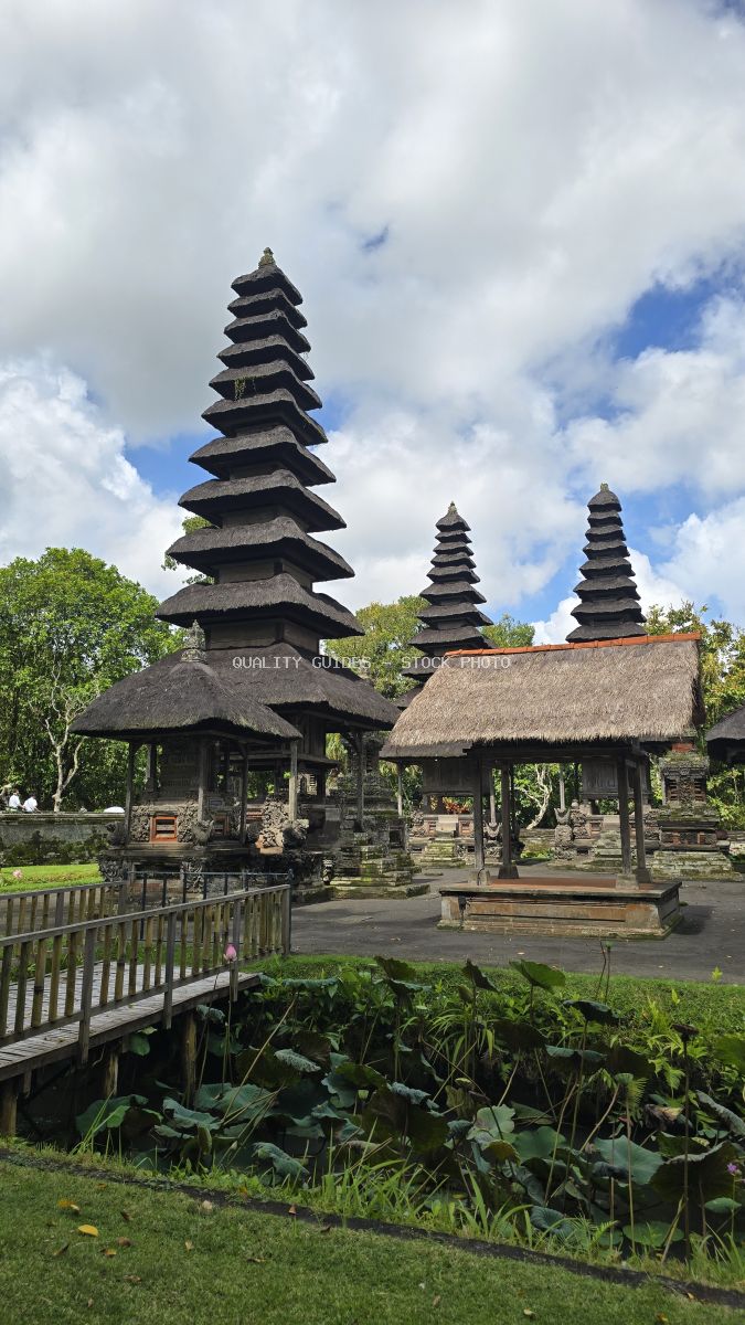Taman Ayun Temple in Bali with traditional multi-tiered pagoda towers and thatched roofs against cloudy sky - stock photo